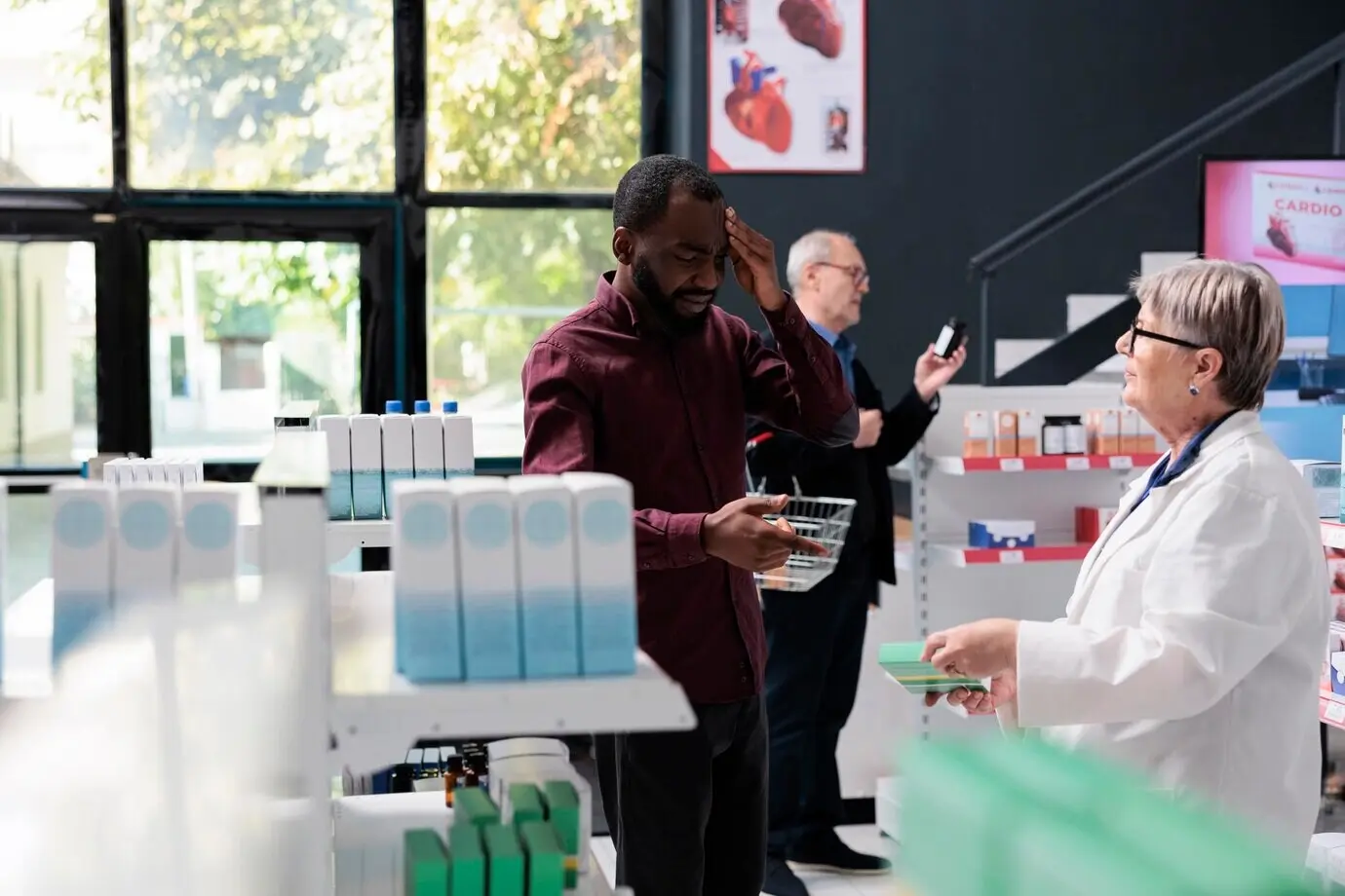 Ein Mann mit starken Kopfschmerzen bittet in der Apotheke einen älteren Apotheker um Migränemedikamente und reibt sich die Schläfen. Der Apotheker hilft dem Kunden mit pharmazeutischen Tabletten. Medizinischer Service.